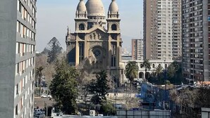 Una gran catedral histórica con tres cúpulas, rodeada de modernos edificios altos.