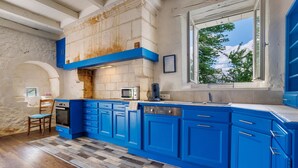 Una cocina con armarios azules, una pared de piedra, un ventanal con vistas y suelo de cuadros.