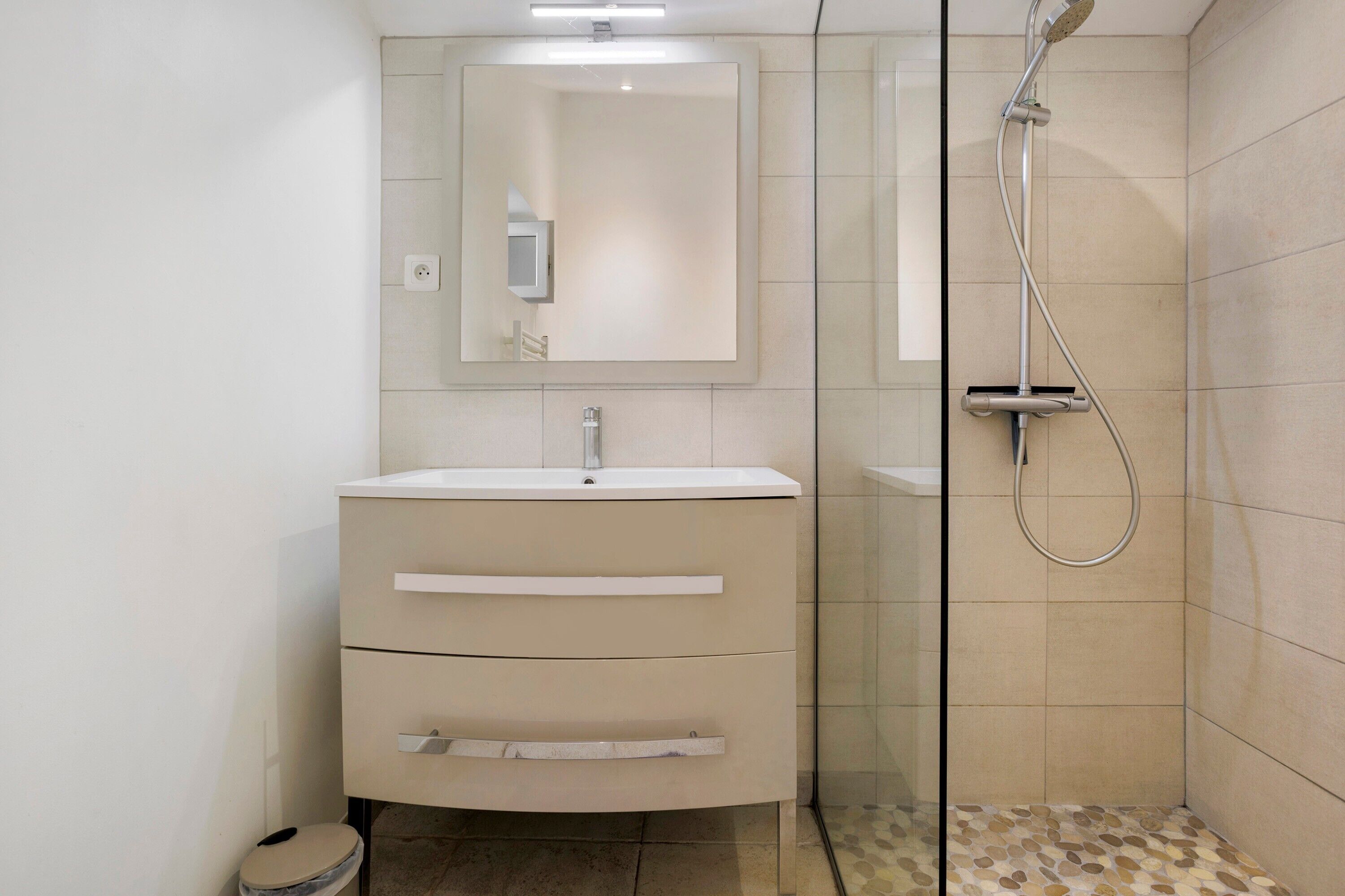 A modern bathroom with a glass shower enclosure, a white vanity with drawers, and a mirror above the sink.
