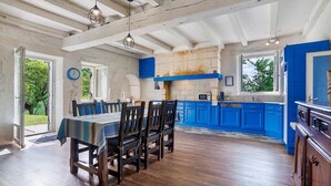 Un comedor con una mesa y sillas de madera, una cocina con armarios azules y un techo rústico.