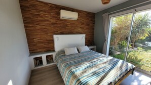 Quarto moderno com parede de madeira, cama grande com roupa de cama listrada e vista para o verde lá fora.
