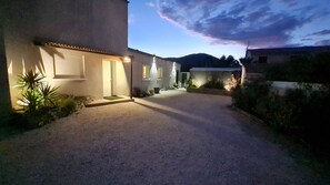 Un camino de grava que lleva a un edificio con una entrada iluminada y un pequeño jardín.