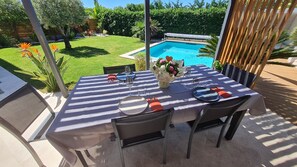 Un área de comedor al aire libre con una mesa lista para dos personas, con vista a una piscina.