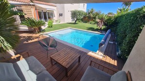 Piscina com deck de madeira, uma cadeira de praia e uma mesa pequena.