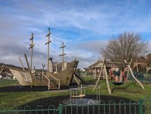 A playground with wooden play structures, including a ship-shaped slide and swings. - 20 Lym Close (Lyme Regis)