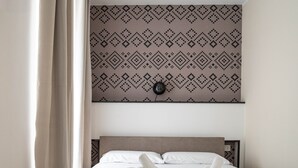 Une chambre d’hôtel avec une tête de lit à motifs, un lit bien fait avec deux serviettes enroulées, et un luminaire fixé au mur.