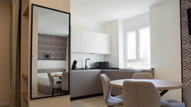 Une chambre d’hôtel moderne dotée d’un coin repas, d’une kitchenette et d’un grand miroir qui reflète la pièce.