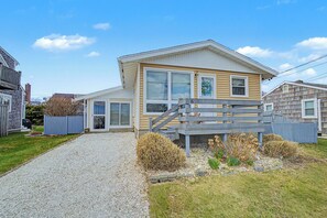A two-story house with a gravel driveway, a wooden deck, and a fenced yard. - 6 Almy Ave (Sandwich)