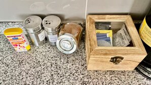 Uma bancada de cozinha com uma caixa de madeira contendo saquinhos de chá, açúcar e um pote de mel.