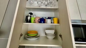 Uma cozinha com um armário embutido contendo diversos utensílios de cozinha, incluindo pratos, canecas e uma cafeteira.