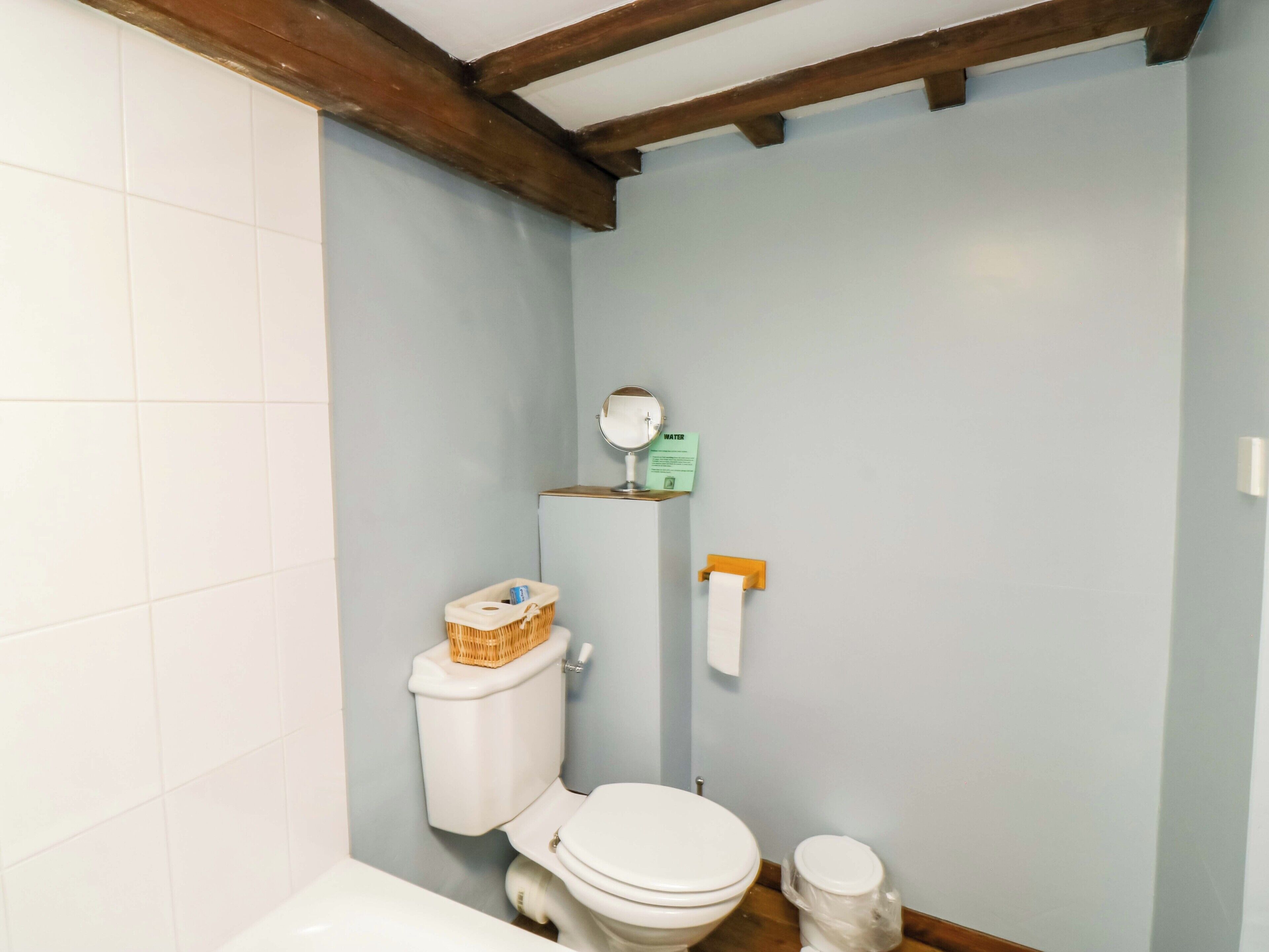 A bathroom with a toilet, a small shelf with a mirror, and a roll of toilet paper.