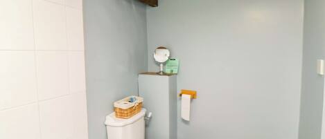 Une salle de bain avec des toilettes, une petite étagère avec un miroir et un rouleau de papier toilette.