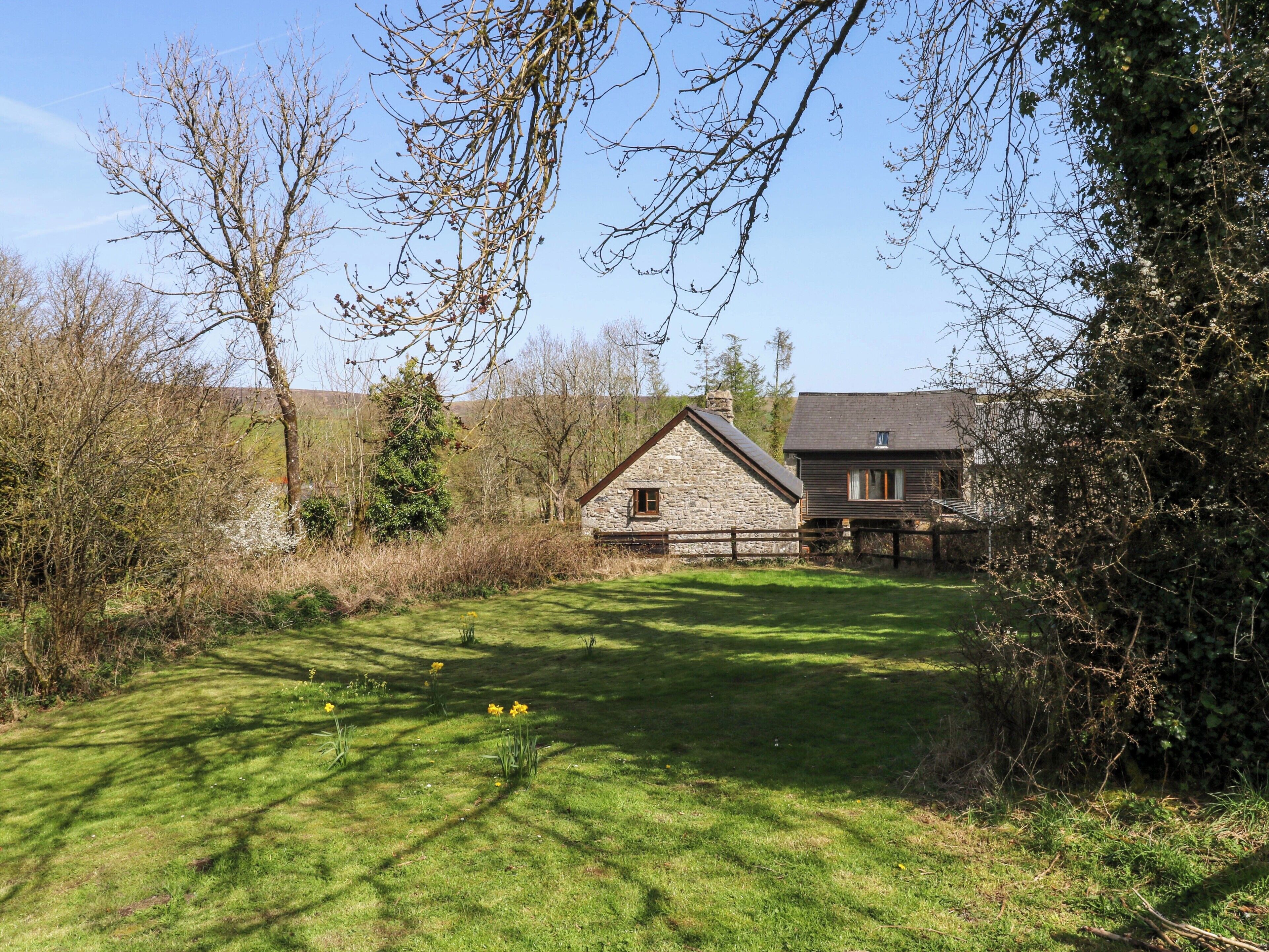 A stone building with a sloped roof, surrounded by a fenced yard with grass and daffodils.