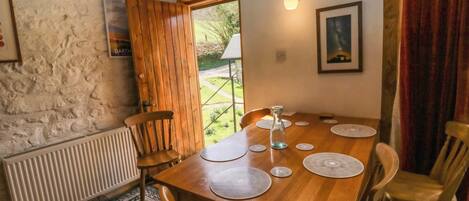 A dining area with a wooden table, chairs, a radiator, a patterned rug, a door, and a wall-mounted light fixture.