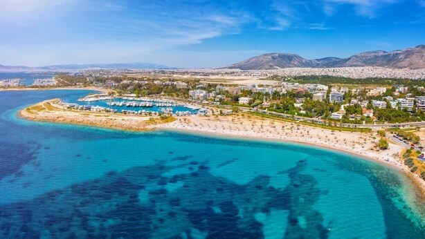 Vista aérea de una zona costera con un puerto deportivo, playa de arena y edificios residenciales.