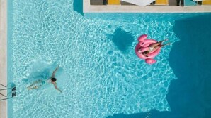 Una piscina con agua azul cristalina, una persona nadando y otra flotando sobre un flotador rosa.