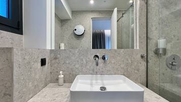 A modern bathroom with a rectangular sink, two faucets, a soap dispenser, and a handheld mirror.