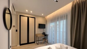 Habitación de hotel moderna con cama, escritorio, televisor y un gran ventanal con cortinas.