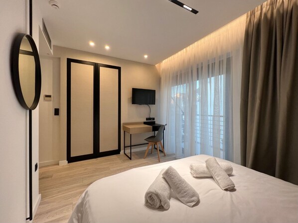 A modern hotel room with a bed, a desk, a TV, and a large window with curtains. - Anghel Hotel (Glyfada)