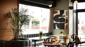 Una cafetería con una planta grande en maceta, muebles modernos y arte abstracto en la pared.