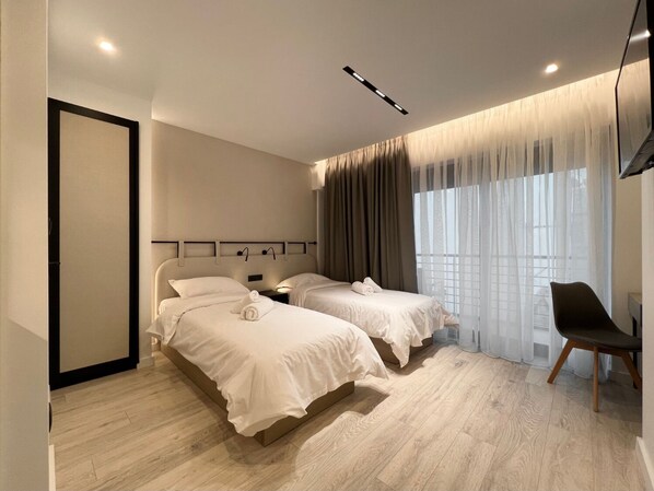 A modern hotel room with two beds, a chair, and a large window with curtains. - Anghel Hotel (Glyfada)