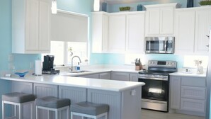 A modern kitchen with white cabinetry, a central island with bar stools, stainless steel appliances, and a blue accent wall. - Your Coastal Getaway:3BR/2BA Beach Retreat (Bolivar Peninsula)