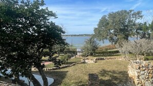 A stone wall, a grassy area, and trees with a body of water in the background.