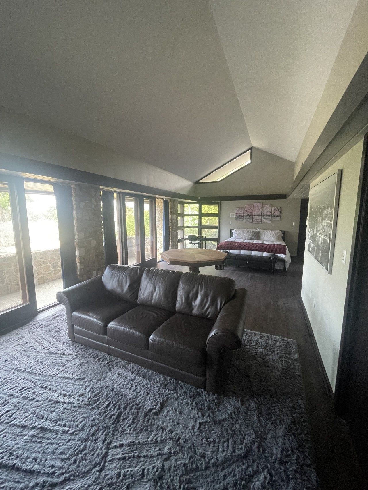 A spacious living room with a leather sofa, a coffee table, and a bed in the background.