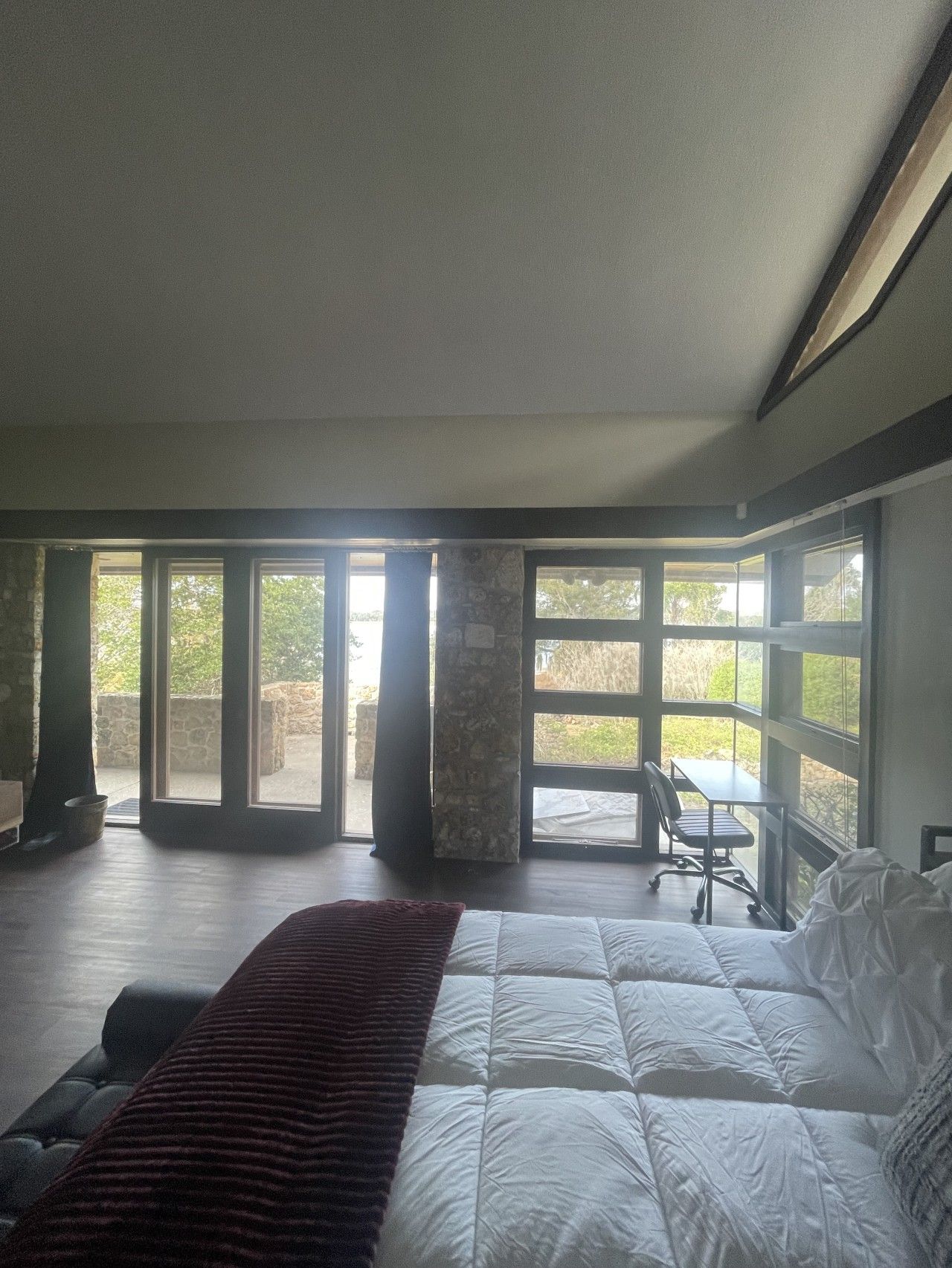 Un dormitorio con una cama grande, un escritorio y vistas a través de las ventanas.