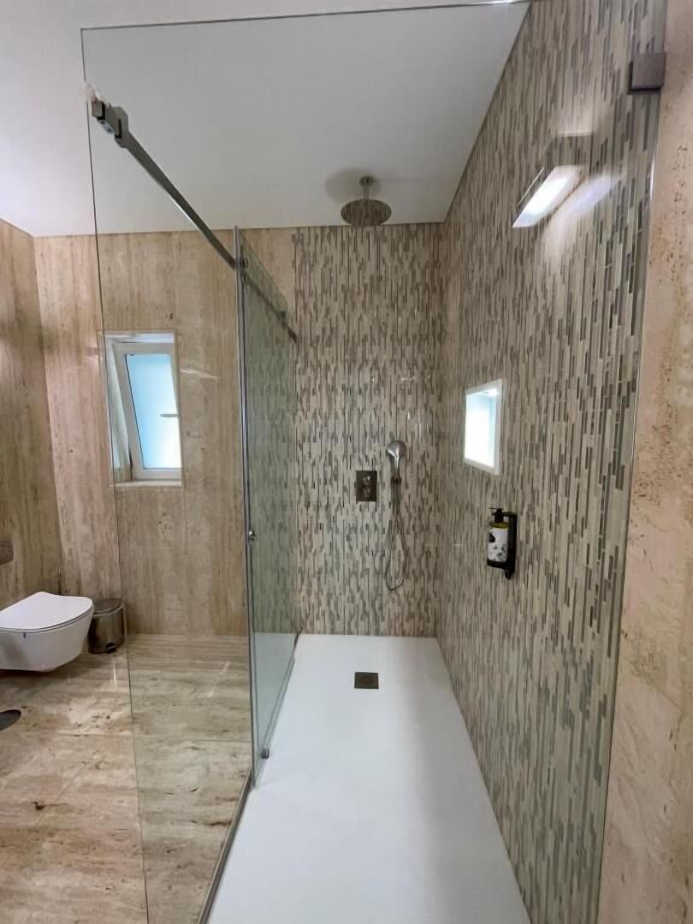 Un baño moderno con cabina de ducha de vidrio, inodoro y un pequeño ventanal.