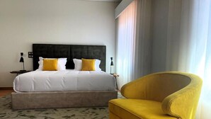 A hotel room with a bed, a nightstand, a lamp, a yellow armchair, and a window with curtains. - Casa de Lamaçais (Paredes)
