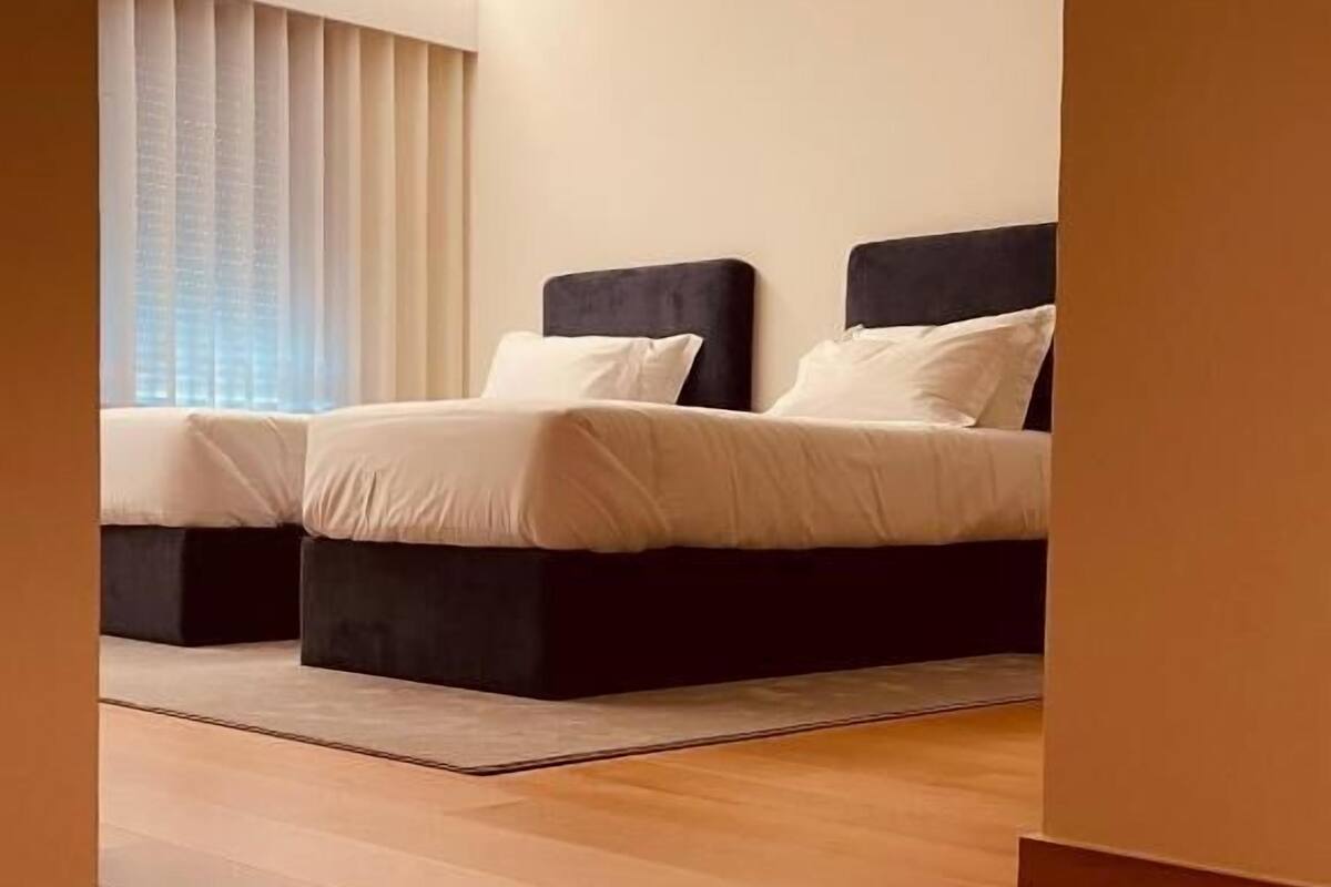 Un dormitorio moderno con una cama grande, una cama más pequeña y una ventana con persianas.