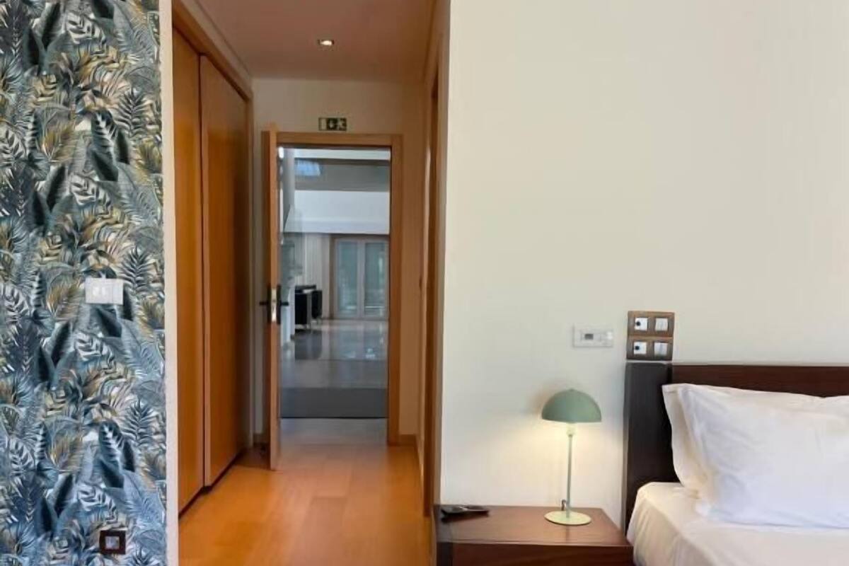 Una habitación de hotel con cama, mesita de noche, lámpara y un papel tapiz estampado.