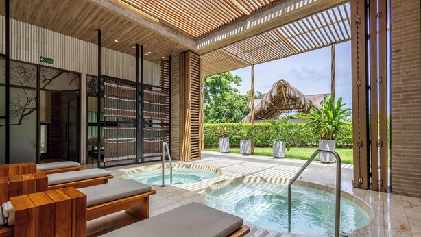 A spa area with wooden loungers, a hot tub, and a view of a thatched-roof structure. - Waterfront escape w/ pool & BBQ grill (Cartagena de Indias)