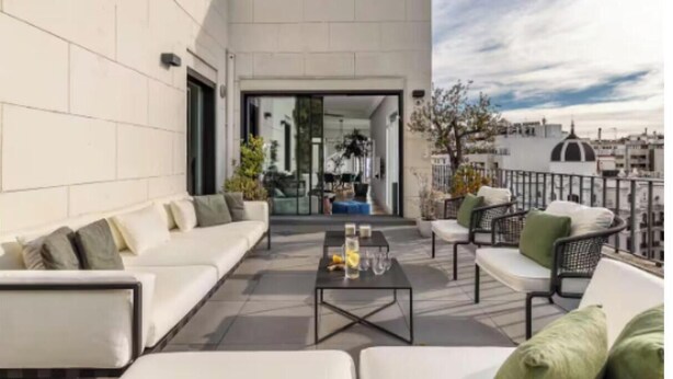 Un espacio exterior moderno con zona de estar, un sofá, sillones, una mesa de centro y vistas a la ciudad.