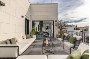 A modern outdoor seating area with a sofa and chairs, a coffee table, and a view of the cityscape. - Luxury 250m² Gran Vía Penthouse with 2 Private Terraces & 360° Views (Madrid)
