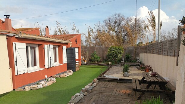 Un immobile residenziale con patio lastricato, piccolo prato e terrazza in legno.