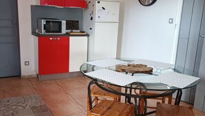 Una cucina compatta con mobili rossi, un frigorifero bianco e un forno a microonde. C'è un tavolo in vetro con quattro sedie di legno e un tappeto decorato sul pavimento.