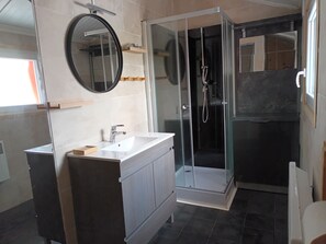 Ein modernes Badezimmer mit einer gläsernen Dusche, einem runden Spiegel und einem weißen Waschbecken.
