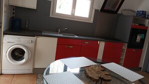Una cucina compatta con lavatrice, una finestra e un'area pranzo con un tavolo rotondo in vetro e tovaglie bianche a pois.