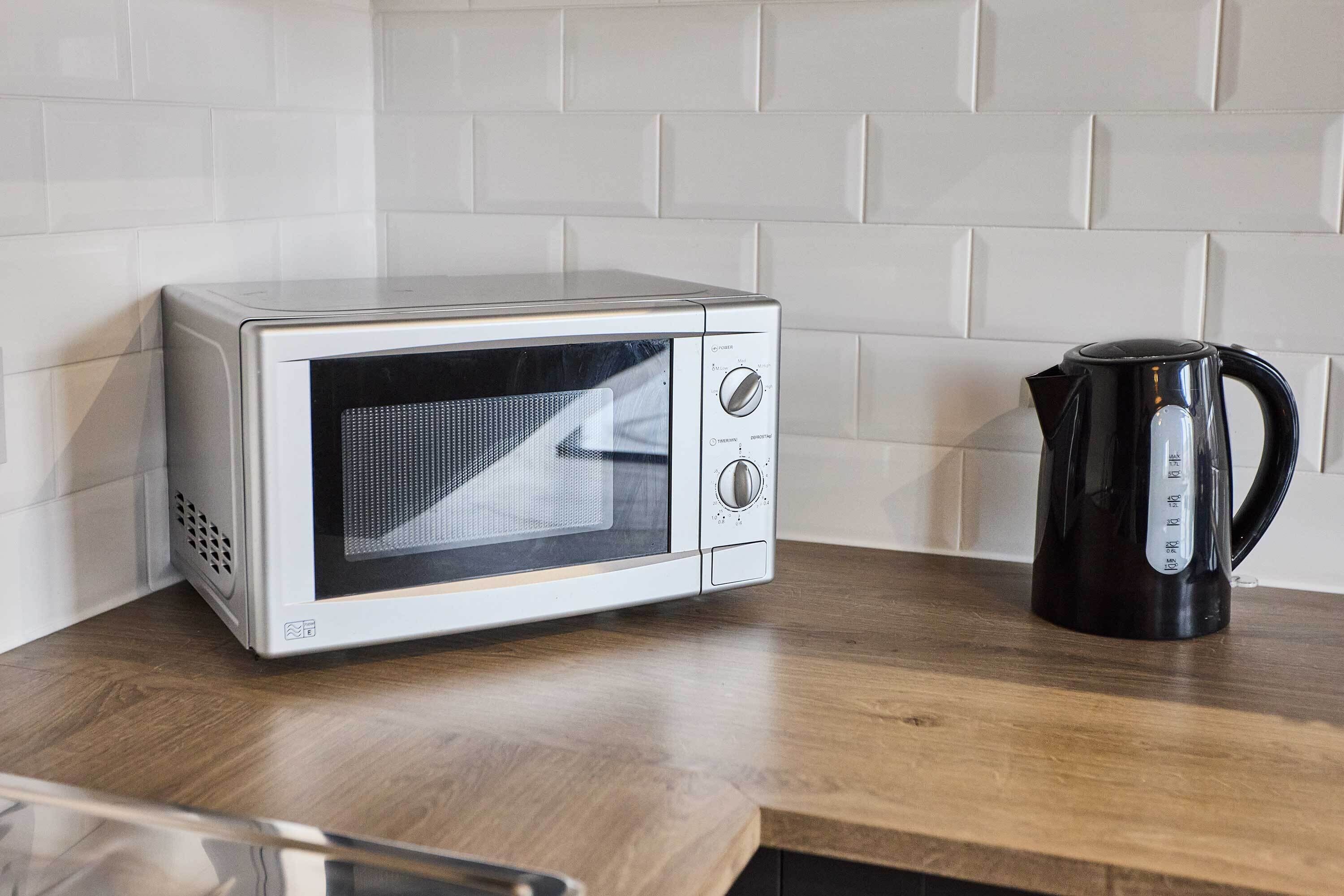 A microwave on a wooden countertop with a black coffee maker beside it.