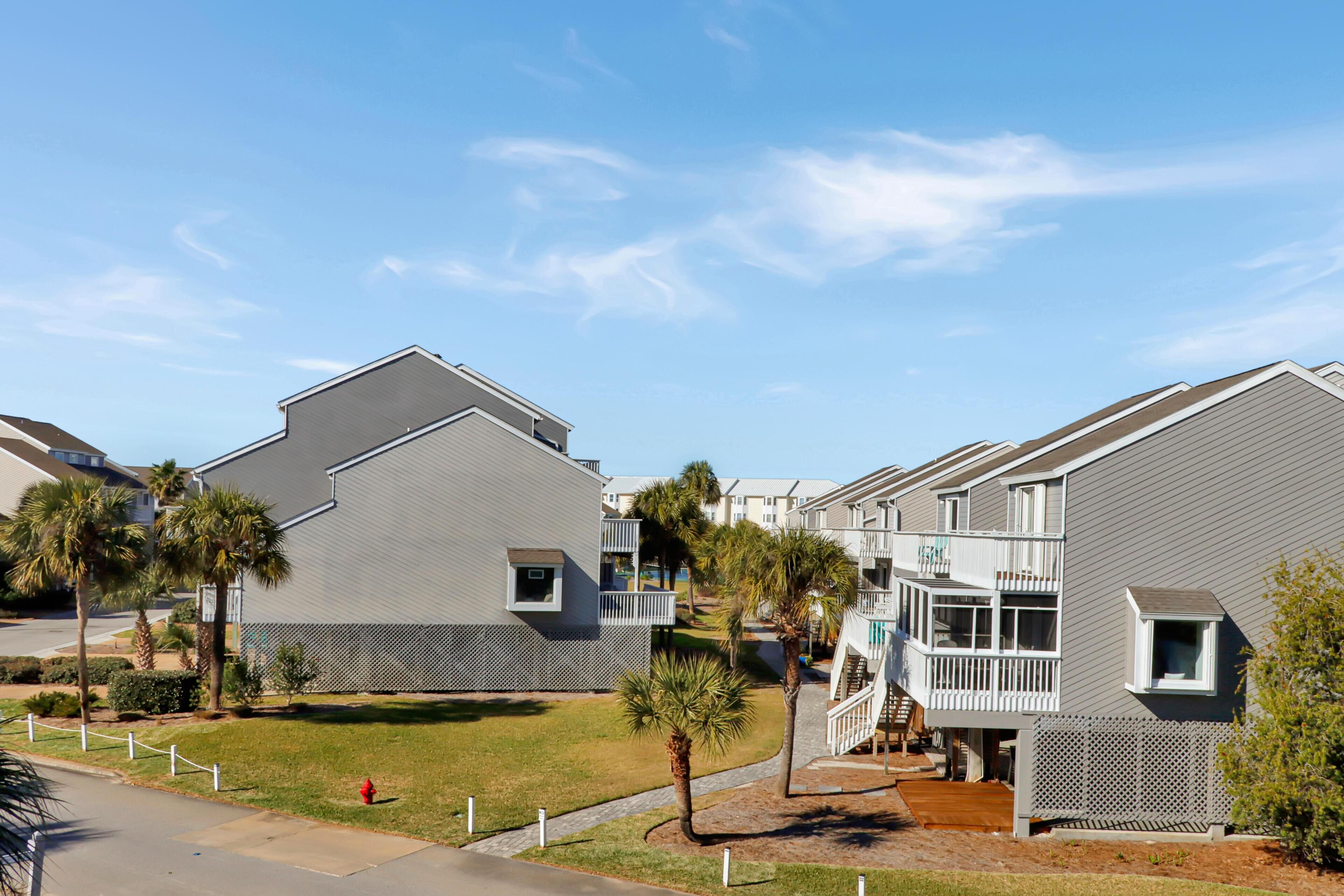A residential building with a grey exterior, a balcony, and a small garden area with palm trees.