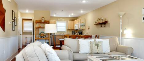 A living room with a beige sofa, a coffee table, and a dining area with wooden chairs and a table.