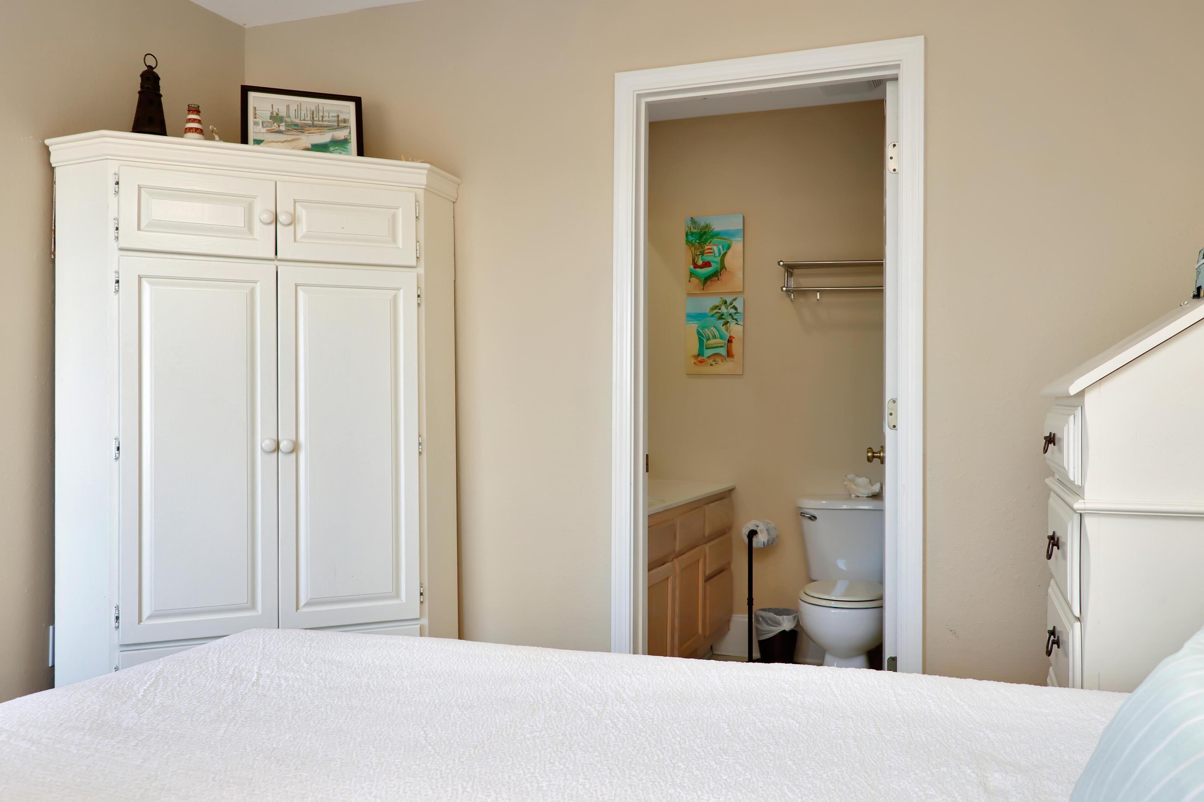 Une chambre à coucher avec un lit, une armoire et une salle de bain visible à travers une porte ouverte.
