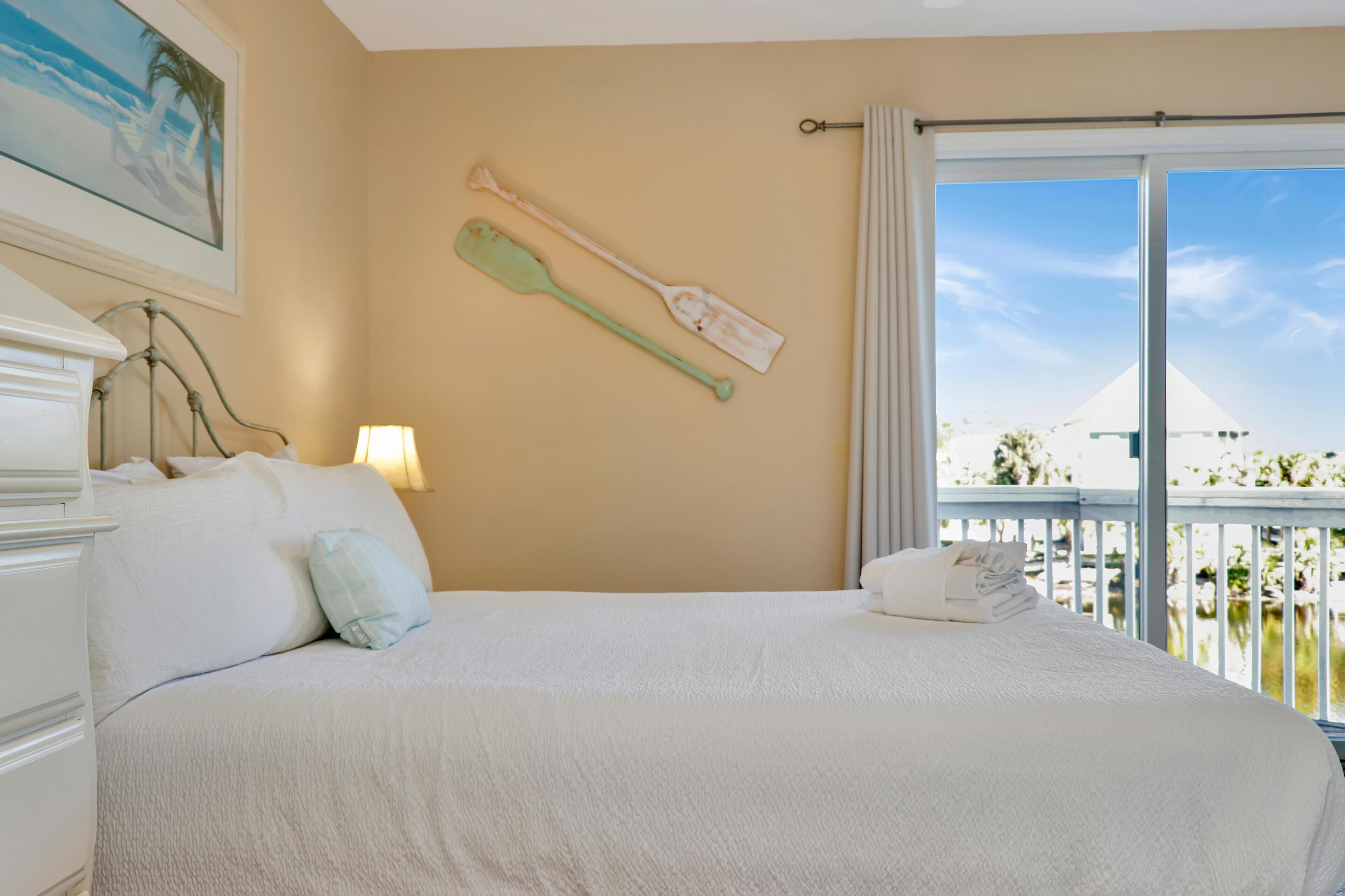 A hotel room with a large bed, a painting on the wall, and a view of a building through the window.