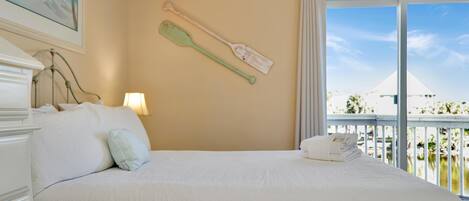 A hotel room with a large bed, a painting on the wall, and a view of a building through the window.