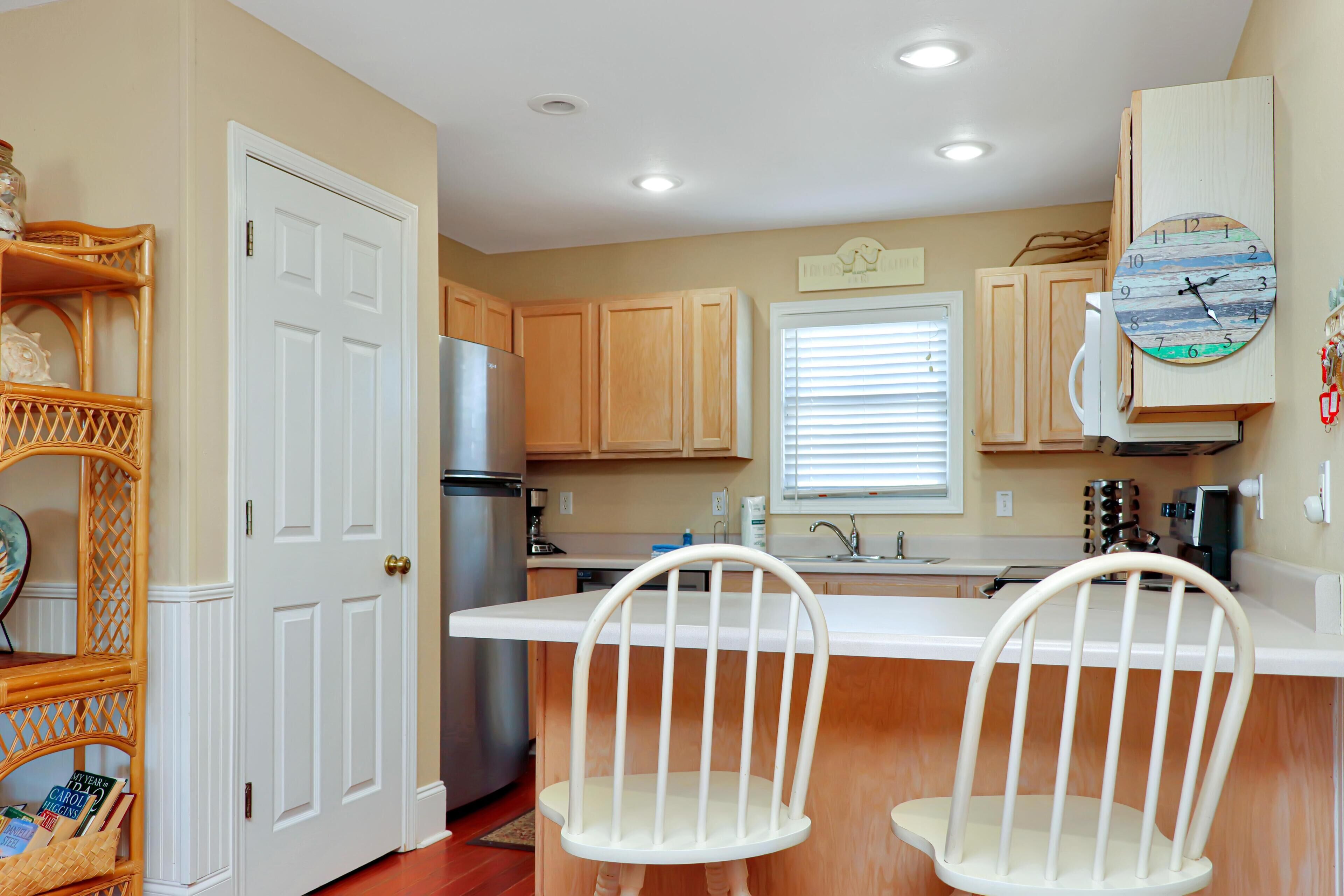 A kitchen with wooden cabinets, a white countertop, a refrigerator, and two white chairs.