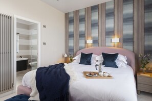 Een moderne hotelkamer met een groot bed, nachtlampjes, een nachtkastje en uitzicht op de badkamer.