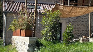 A rustic stone building with a tiled roof, a wooden pergola, and a garden area with plants and a wooden planter. - Gîte Métairie la Faurie in the heart of Drôme (Aurel)