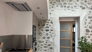 A kitchen with a modern stove, a stone wall, and a wooden door leading to another room. - Gîte Métairie la Faurie in the heart of Drôme (Aurel)